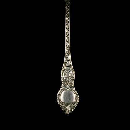 engraved antique silver teaspoon. vintage cutlery for table setting with floral pattern on black isolated backgroundの写真素材