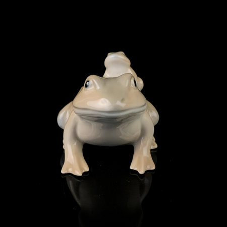 Frog ceramic figurine isolated on black background, side view. antique porcelain figurine of a frogの写真素材