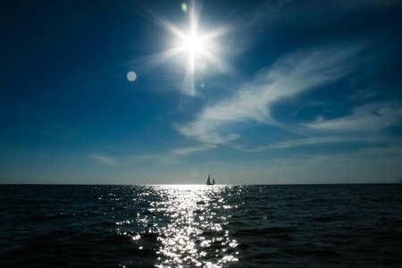 A lonely sail boat and the sun in the dramatic sky is sailing in the seaの写真素材