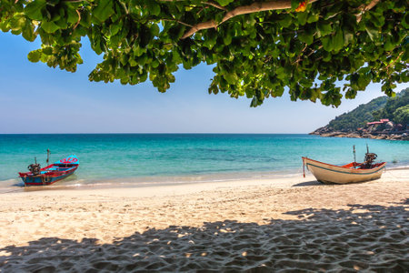 Two motor boats at the tropical beach with white sand. Vibrant blue calm sea and leelawadee tree. Phangan, Thailand.の写真素材