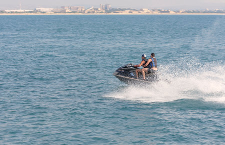 Acre, Israel - 11.05.2018: Sports active rest on the Mediterranean sea. Two young men racing on jet ski. Active summer vacation. Background is the panorama of city Acreのeditorial素材