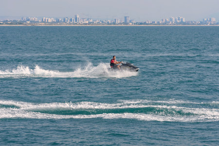 Acre, Israel - 11.05.2018: Sports active rest on the Mediterranean sea. Young man racing on jet ski, water scooter. Active summer vacation. Background is the panorama of city Acreのeditorial素材