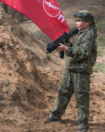 Novgorod, Russia - 04 September 2016: Boy in camouflage with a laser tag pistol. Classmates play together outdoors. Active sport leisure. Vertical photoのeditorial素材