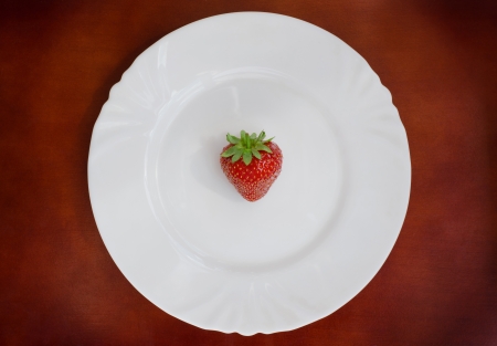 Single fresh strawberry on white plate over brown backgroundの写真素材