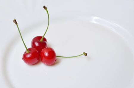 Three red cheries on a white plate