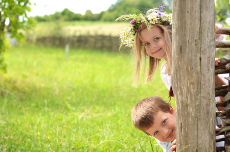 Little boy and girl peeking of the wooden fence in summerの写真素材