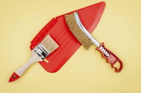 Construction tool on a yellow background. Repair tool. Metal brush, spatula for smoothing wallpaper and paint brush. Background mode. Accessories painter.の写真素材