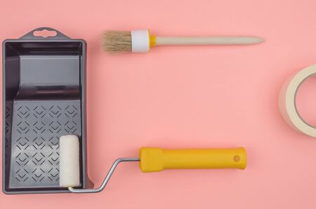 House painter tool on a pink background. Paint roller, brush, paint cuvette and masking tape.