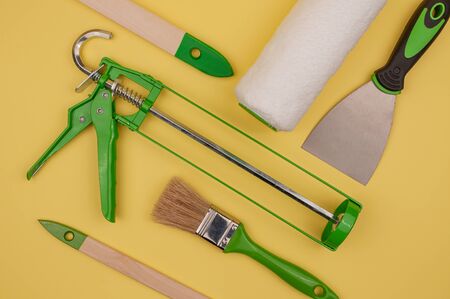 Green paint hand tool on a yellow background. Brush and putty knife, paint roller and gun.の写真素材