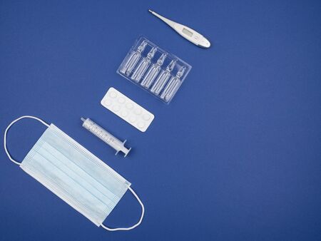 Mask, syringe, thermometer, tablets and capsules on a blue background. The view from the top.