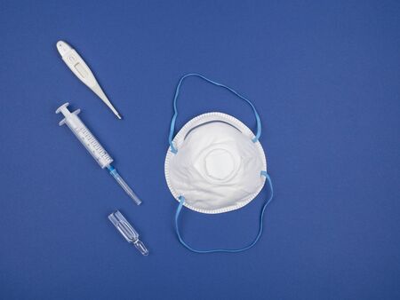 Respirator, syringe, ampoule, and an electronic thermometer on blue background. The view from the...
