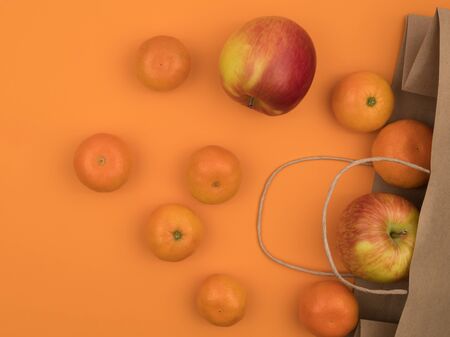 Tangerines and apples in a ecological paper bag. Orange background. The view from the top. Organic fruits.の写真素材