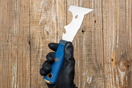 A hand firmly grasping a unique and finely crafted blade tool set against a rustic wooden backdropの写真素材