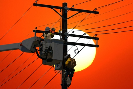 Utility workers repair a power line at sunsetの写真素材
