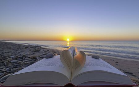 Zen on the beach. Book folded in the shape of a heart with sunrise.の写真素材