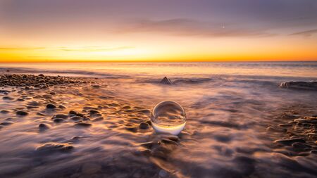 Crystal ball on pebbles of a beach at sunrise.の写真素材