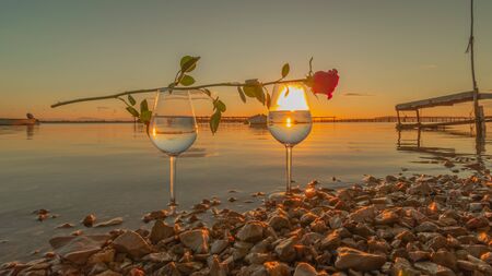 Wine glass with a red rose and with reflections of a sunset over the sea.の写真素材