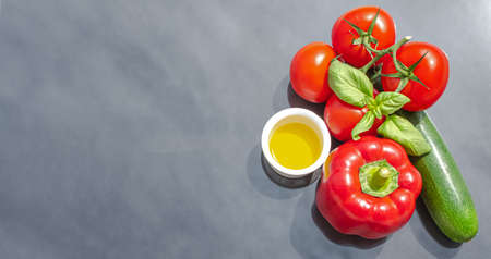 Creative presentation of summer seasonal vegetables with tomatoes, zucchini, red pepper, olive oil and fresh basil. On background to include text.の写真素材