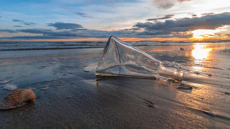 Glass bottle washed up on a beach with reflections on the sand and sunset.の写真素材