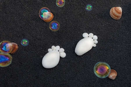 Sea sand grains background, fine black beach sand. Space for text. Pebbles in the shape of a small foot to announce a birth.の写真素材