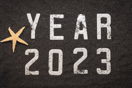 Happy new year 2023 concept with seashell and starfish on black beach sand. Winter vacation in the sun.の写真素材