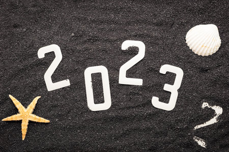 Happy new year 2023 concept with seashell and starfish on black beach sand. Winter vacation in the sun.の写真素材