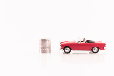 Miniature people: Businessman riding a red car with stack of coins on white backgroundの写真素材