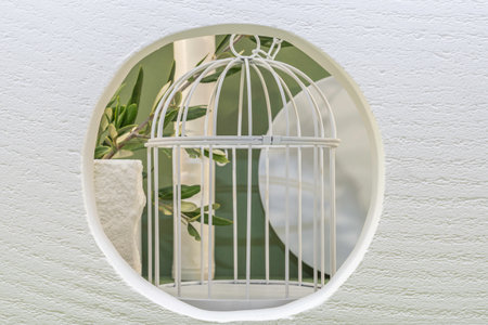 White metal bird cage with green leaf inside on white wall background.