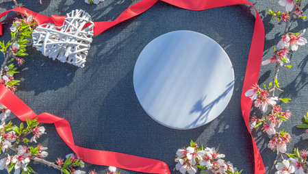 White round plate with red ribbon and heart on black fabric background.の写真素材