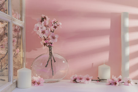 Glass vase with pink flowers and candles on the table in the roomの写真素材