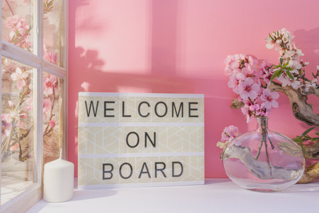 Welcome on board with flowers in vase on table, pink backgroundの写真素材