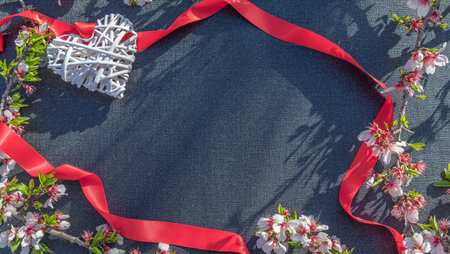 Frame of red ribbons, hearts and flowers on black fabric background