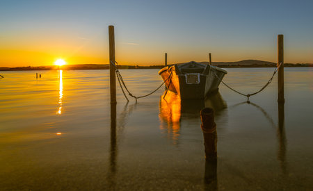 A boat is tied up at a dock on a calm lake at sunset.の写真素材