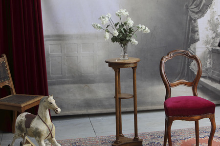 typical old photo studio with chair, table, flowers, rocking horse and a marble balustradeの写真素材
