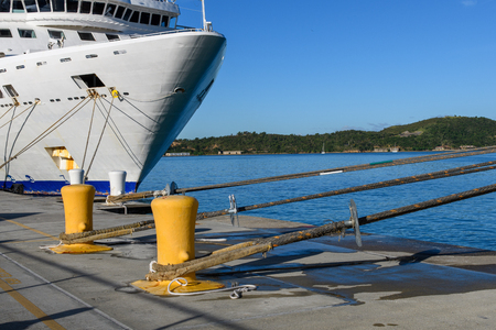 The bow of the white cruise ship standing at the pier. Ropes, berth, blue sea and wooded shore.の写真素材