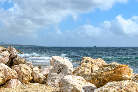 Seascape with huge rocks in the foreground, surf waves, ship silhouette on the horizon and blue sky with clouds.の写真素材