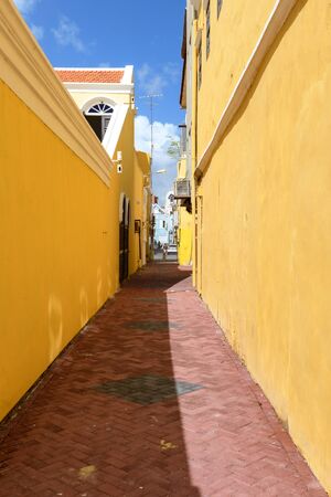 A narrow street of a medieval town with bright yellow walls, a brown granite pavement against the blue sky stretching into the distanceの写真素材