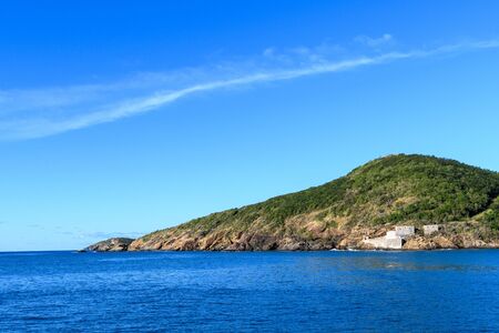Sea view of a tropical island against a cloud that follows the shape of a hill on the island. Green tropical island with the remains of an ancient fortress on the shore.の写真素材