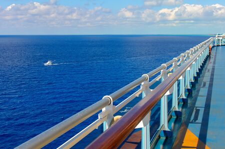 Going into the distance in the perspective of the railing of the deck of the ship on the background of the blue ocean and a white motor yacht on the waves.の写真素材