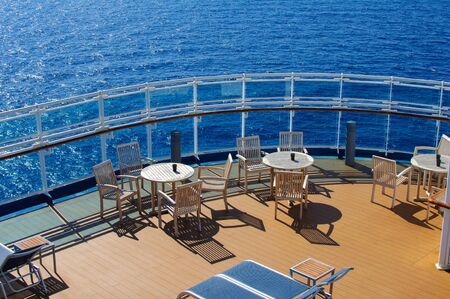 White dining tables with chairs and sun loungers on the deck of the ship against the blue ocean in Sunny weather.の写真素材