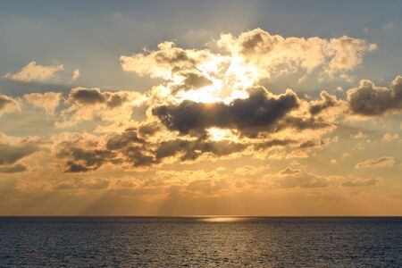 Illuminated by the setting sun clouds over the sea horizon with rays of light and glare on the water.の写真素材