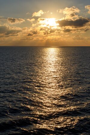 Illuminated by the setting sun clouds over the sea horizon with rays of light and glare on the water.の写真素材