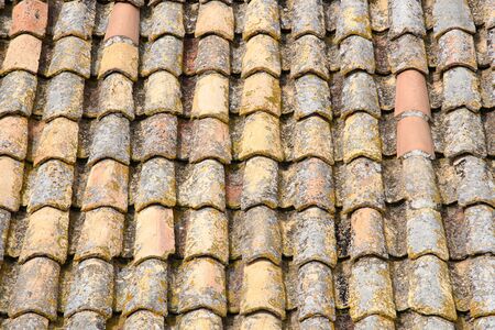 A fragment of an old tiled roof covered with mold and traces of time. Aged shingles. Background. Pattern. Terracotta. Gray. Ocher.の写真素材
