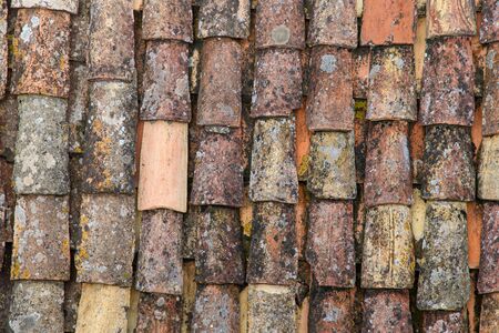 A fragment of an old tiled roof covered with mold and traces of time. Aged shingles. Background. Pattern. Terracotta. Gray. Ocher.の写真素材