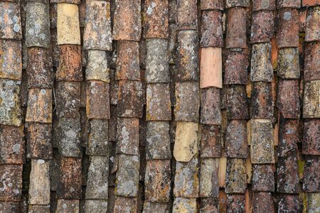 A fragment of an old tiled roof covered with mold and traces of time. Aged shingles. Background. Pattern. Terracotta. Gray. Ocher.の写真素材