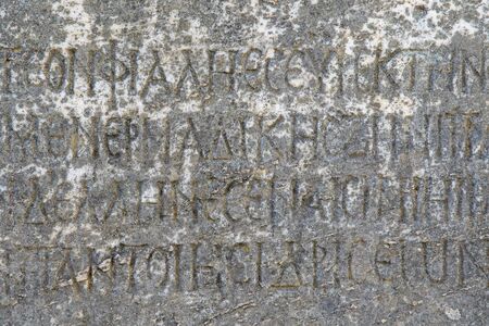 Half-erased ancient Greek letters embossed on an old gray marble slab covered with cracks and mold.の写真素材