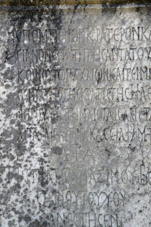 Half-erased ancient Greek letters embossed on an old gray marble slab covered with cracks and mold.の写真素材