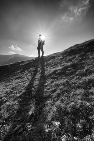 Heroic silhouette of a photographer and trekker in front of a dramatic sunstarの写真素材