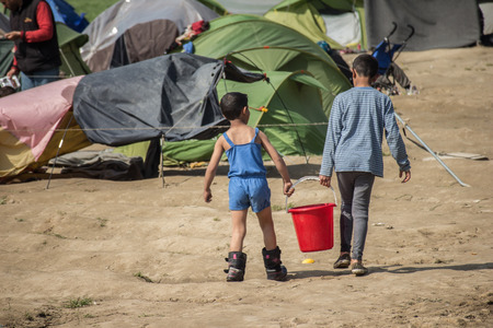 Idomeni, Paeonia, Kilkis regional unit of Central Macedonia / Greece - March 22 2016: two kids carrying a bucket of water in the tents where they live in the refugee camp of Idomeni.のeditorial素材