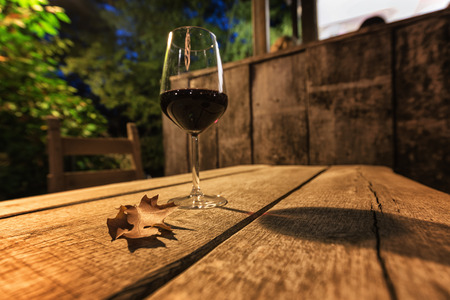 A glass of red wine and a brown autumn leaf on a wooden table in Friuli, Italy.の写真素材